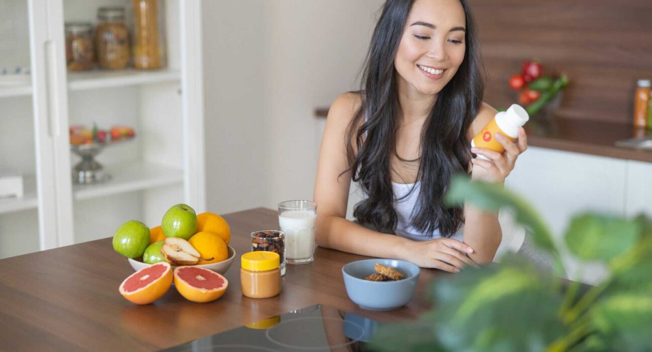 Kobieta sięgająca po suplement diety przy śniadaniu – codzienna suplementacja i świadomy wybór produktów