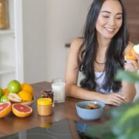 Kobieta sięgająca po suplement diety przy śniadaniu – codzienna suplementacja i świadomy wybór produktów